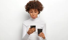 A woman holding a cup of coffee while looking at her phone.