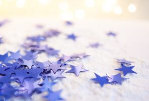 Blue star-shaped confetti scattered on a white surface with soft glowing lights in the background.