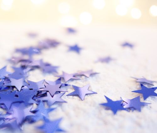 Blue star-shaped confetti scattered on a white surface with soft glowing lights in the background.
