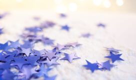 Blue star-shaped confetti scattered on a white surface with soft glowing lights in the background.