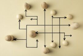 Wooden balls placed on a beige background with black arrows and lines creating a complex interconnected pathway.