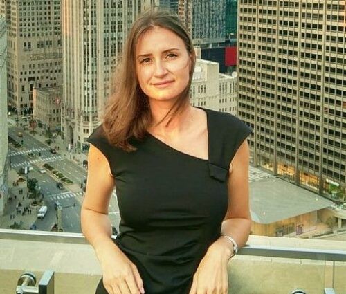 A woman in a black dress stands on a balcony overlooking a cityscape with tall buildings and a busy street below, contemplating test optimization strategies.