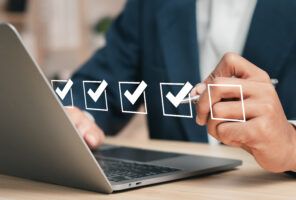 A person in a suit using a laptop completes digital checkboxes with a checkmark in each of four boxes and a fifth unchecked box, marking progress or a checklist task, demonstrating effective test optimization.