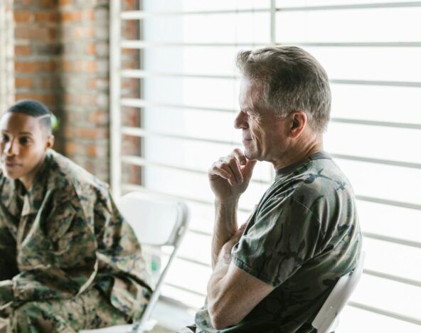 Two people in military uniforms are seated indoors. One is in the foreground, while the other, in the background, is looking away pensively, as if considering how generative AI might influence future strategies.