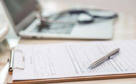 A clipboard with a medical form and a pen lies on a desk next to an open laptop and a stethoscope, illustrating how generative AI is revolutionizing healthcare documentation.