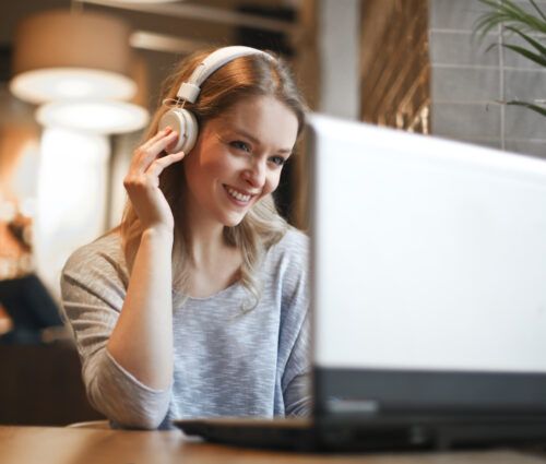 Woman with headphones smiling while looking at a laptop in a cozy, softly lit room, immersed in automated accessibility testing.