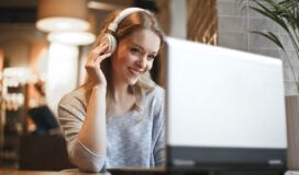 Woman with headphones smiling while looking at a laptop in a cozy, softly lit room, immersed in automated accessibility testing.