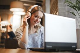 Woman with headphones smiling while looking at a laptop in a cozy, softly lit room, immersed in automated accessibility testing.