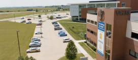 Aerial view of the exterior of a modern, multi-story office building with a sign reading "VGM Group" and a parking lot with multiple cars. Manicured lawns surround the area, and fields are visible in the distance—the hub for innovative machine learning advancements.