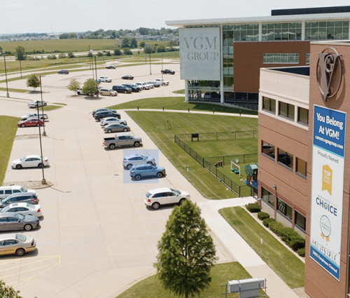 Aerial view of the exterior of a modern, multi-story office building with a sign reading "VGM Group" and a parking lot with multiple cars. Manicured lawns surround the area, and fields are visible in the distance—the hub for innovative machine learning advancements.