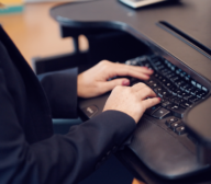 A person in a dark suit types on a black keyboard at a desk, seamlessly integrating machine learning algorithms into their work.