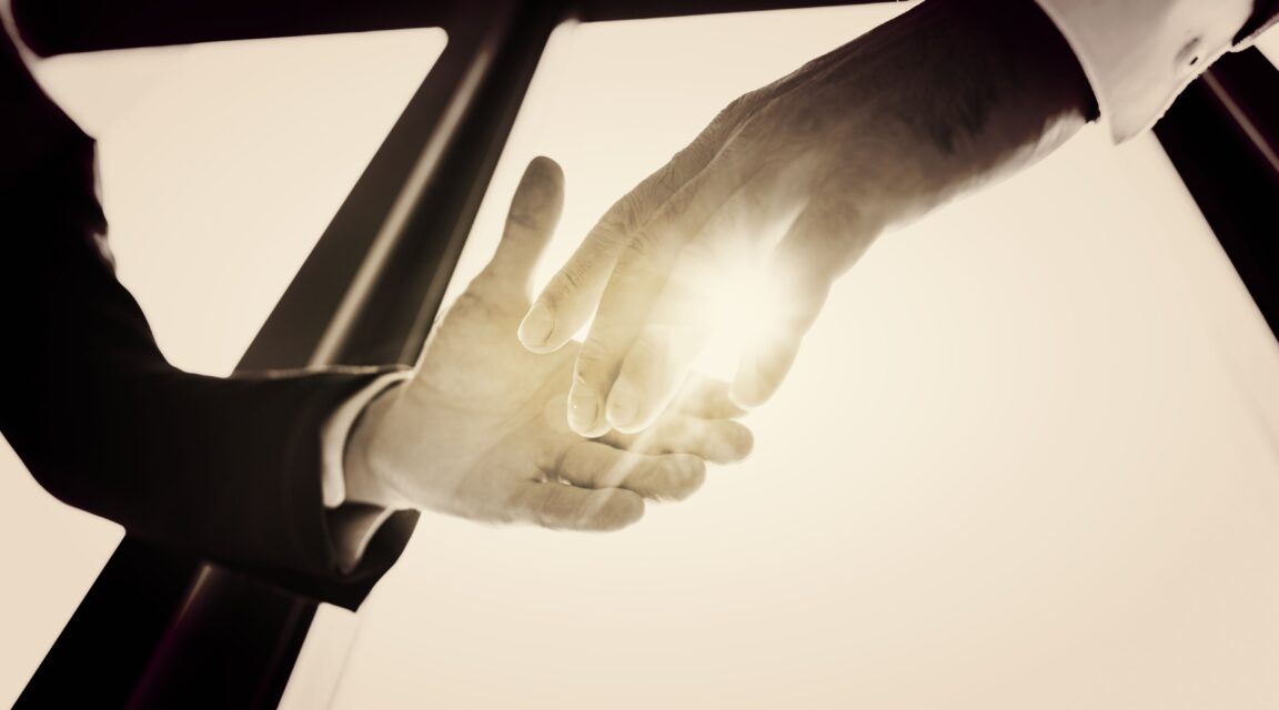 Two hands reaching towards each other with sunlight shining between them, set against a windowed backdrop, symbolize the synergy of tech leadership.