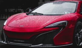 A red sports car with raindrops on its surface is parked outdoors.