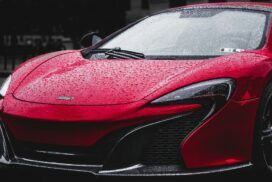 A red sports car with raindrops on its surface is parked outdoors.