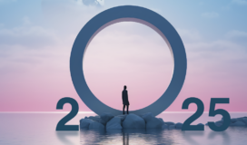 A person stands on rocks in front of a large ring between the numbers 2025, symbolizing the dawn of tech predictions, set against a pink and blue sky over water.