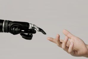 A robotic hand and a human hand reach towards each other against a neutral background.