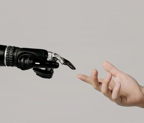 A robotic hand and a human hand reach towards each other against a neutral background.