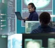 Two people work in a high-tech control room with multiple monitors displaying code, digital maps, and Secure LLM interfaces.