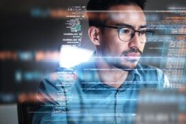 A man wearing glasses looks at a computer screen displaying lines of code, suggesting he is working on programming or developing SaaS applications.