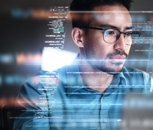 A man wearing glasses looks at a computer screen displaying lines of code, suggesting he is working on programming or developing SaaS applications.