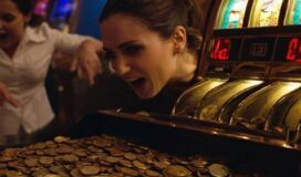 A woman leans close to a slot machine overflowing with coins, appearing excited while another person reacts enthusiastically in the background.