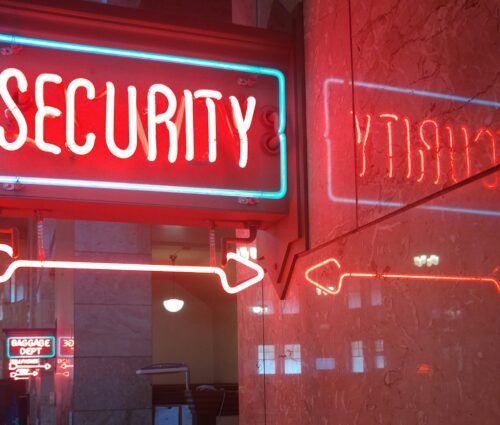 A red neon sign reading "SECURITY" with arrows, symbolizing enterprise AI security, is reflected on a marble wall. In the background, another neon sign reads "BAGGAGE DEPT.
