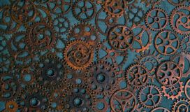 A collection of variously sized, rusty metal gears and cogs arranged closely together on a textured blue surface, evoking the intricate mechanics behind AI agent development lessons.