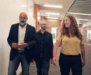 Three people, two men and one woman, walk together down a modern office hallway, engaged in conversation.