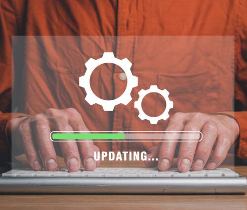 Person wearing an orange shirt typing on a keyboard, with a transparent graphic overlay showing gears and a progress bar labeled "UPDATING...