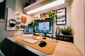 A neatly organized home office desk with a laptop, monitor, keyboard, mouse, plants, headphones, and a sign that reads "NO BAD DAYS.
