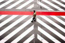 A person walks across a crosswalk with bold white diagonal lines and a single red horizontal stripe, as AI software monitors traffic for enhanced safety.