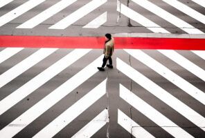 A person walks across a crosswalk with bold white diagonal lines and a single red horizontal stripe, as AI software monitors traffic for enhanced safety.
