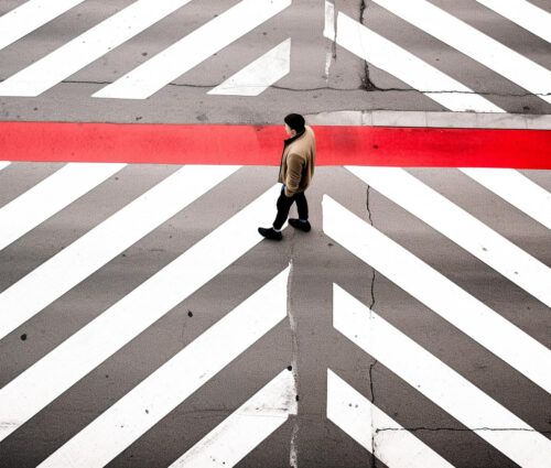 A person walks across a crosswalk with bold white diagonal lines and a single red horizontal stripe, as AI software monitors traffic for enhanced safety.