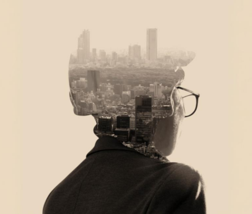 A person wearing glasses is seen from behind, with a cityscape superimposed within the silhouette of their head and shoulders.