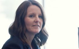 A woman with shoulder-length brown hair and a navy blazer sits indoors, looking toward the camera with a neutral expression, suggesting confidence in her expertise in ML for insurance.