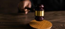 A person holds a wooden gavel above a sound block on a wooden table, symbolizing a judicial setting informed by a generative AI court analysis system.