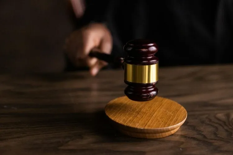 A person holds a wooden gavel above a sound block on a wooden table, symbolizing a judicial setting informed by a generative AI court analysis system.